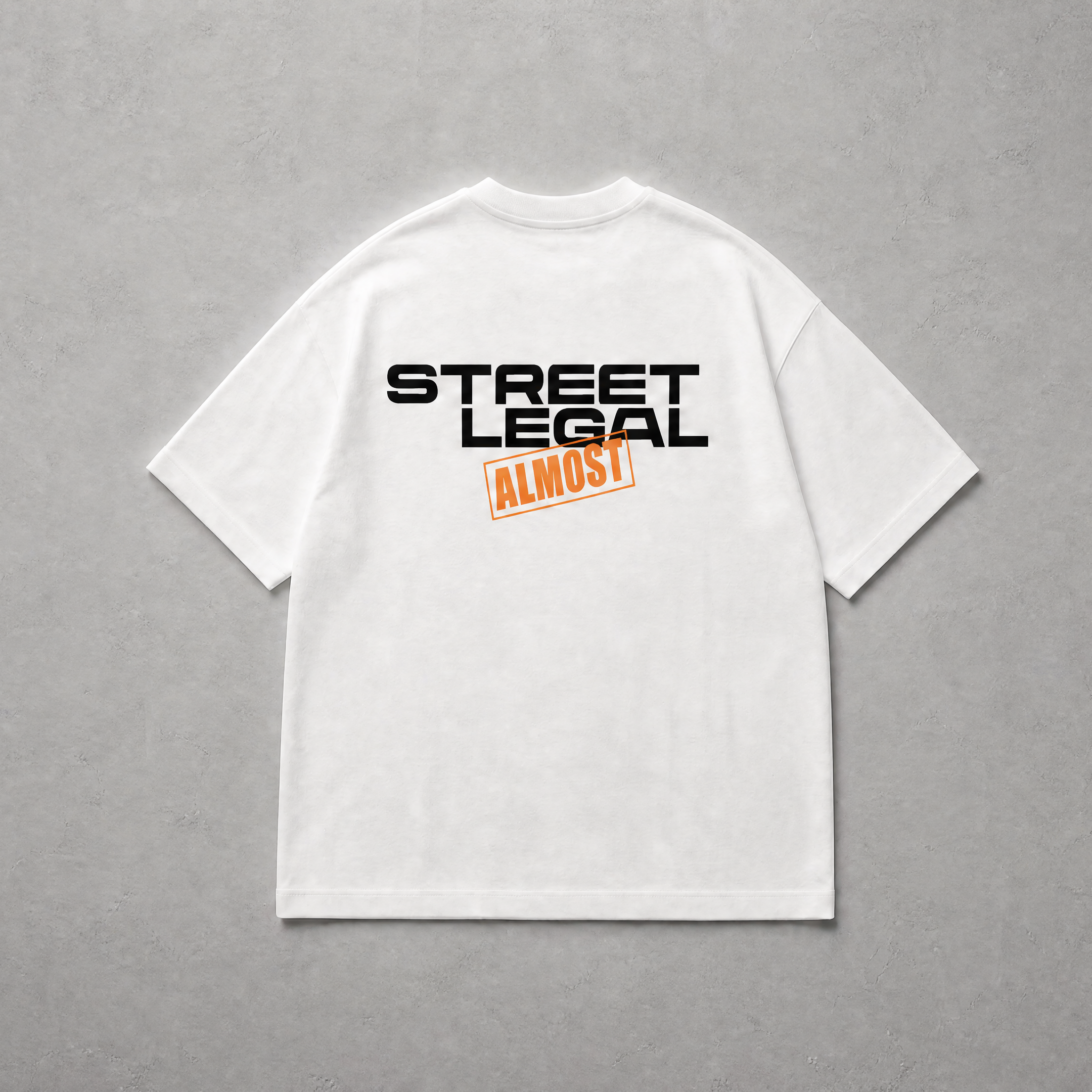 A white short-sleeve t-shirt shown from the back, featuring a graphic print with the words 'STREET LEGAL' in black and 'ALMOST' in orange. The t-shirt is laid flat on a textured gray background.