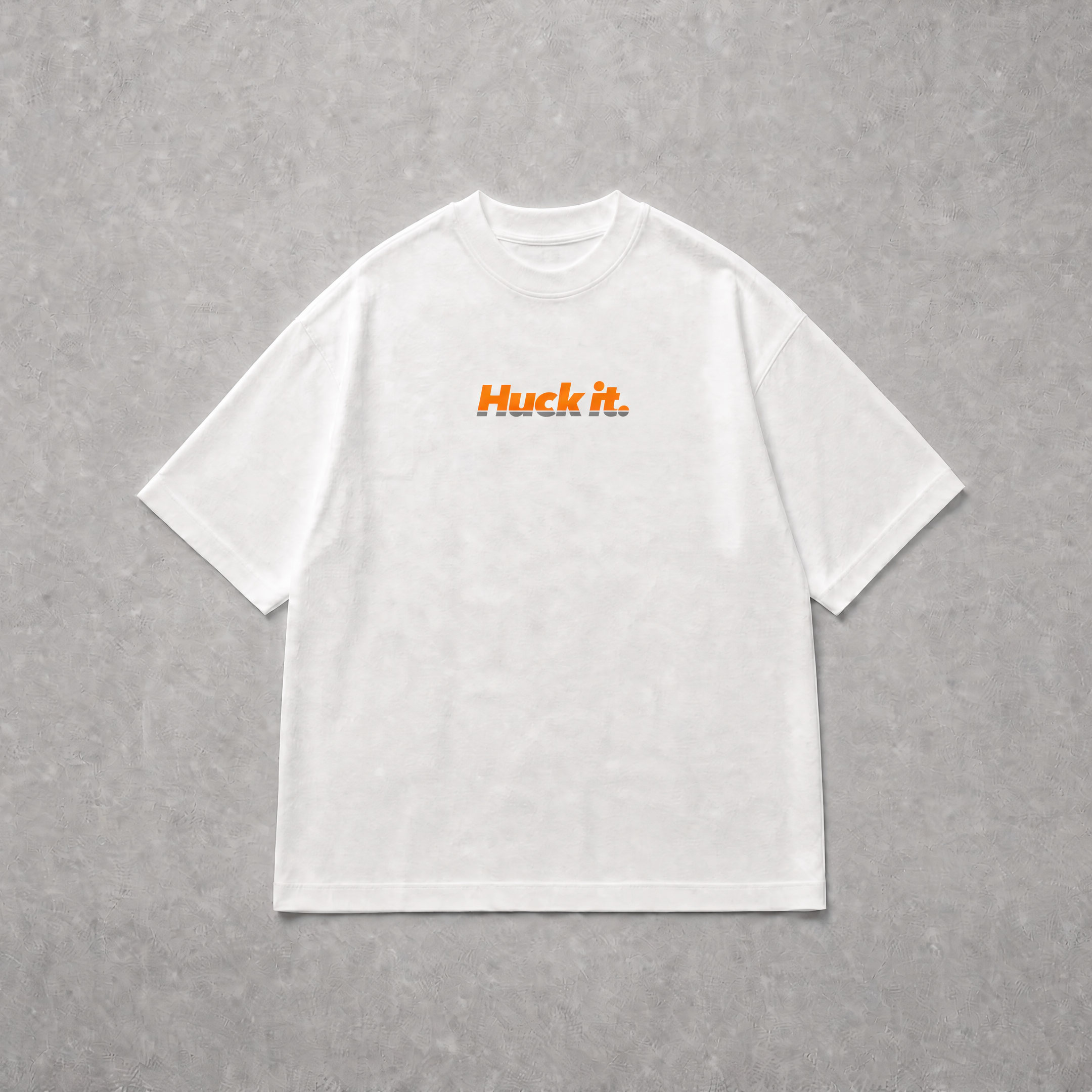 A white short-sleeve crewneck t-shirt with the text 'Huck it.' printed in orange across the chest, laid flat on a textured grey background.