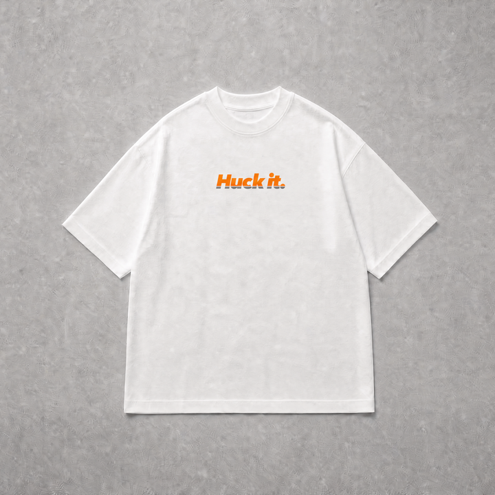 A white short-sleeve crewneck t-shirt with the text 'Huck it.' printed in orange across the chest, laid flat on a textured grey background.