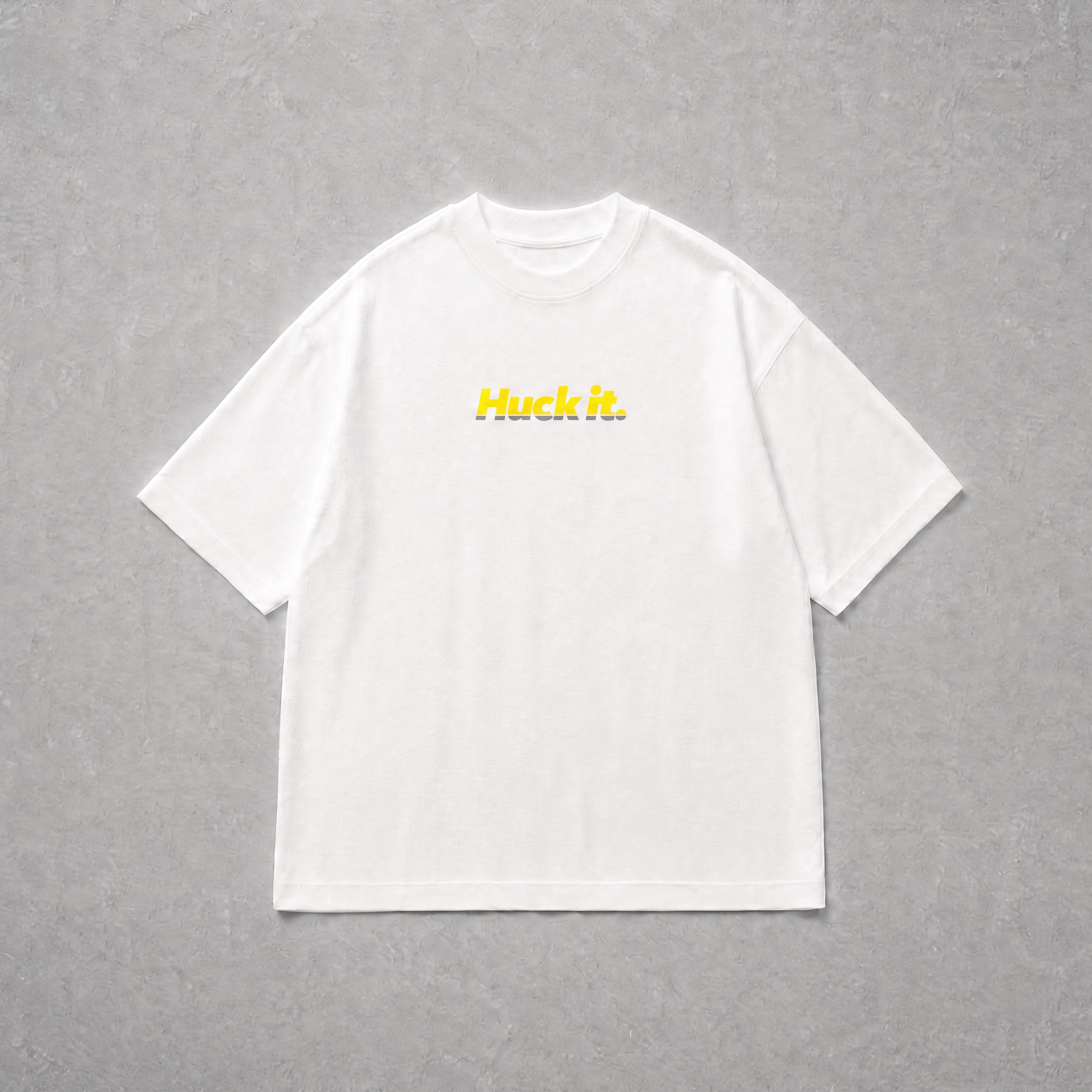 A white short-sleeve crewneck t-shirt with the word 'Huck it.' printed in yellow across the chest, laid flat on a textured gray background.