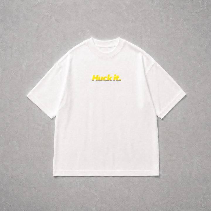 A white short-sleeve crewneck t-shirt with the word 'Huck it.' printed in yellow across the chest, laid flat on a textured gray background.