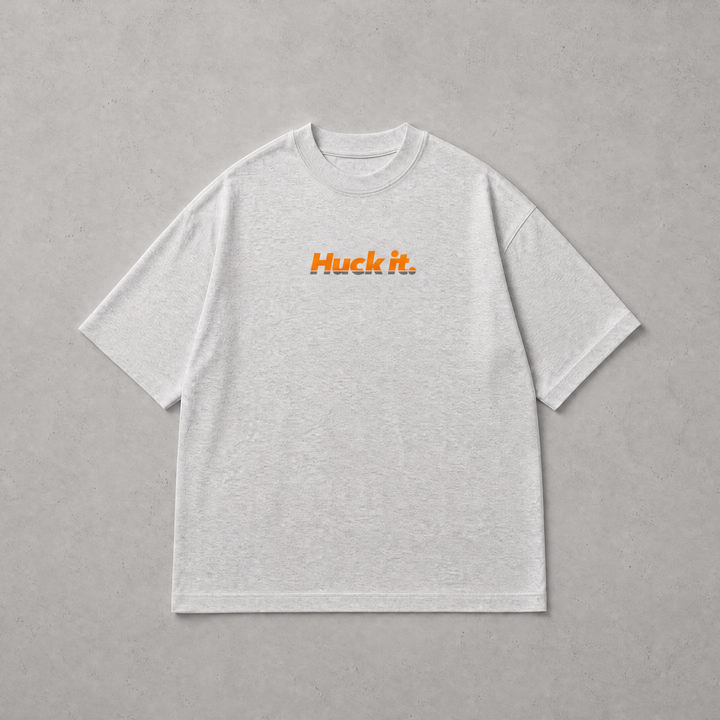 A light gray heather crewneck t-shirt with the text 'Huck it.' printed in orange across the chest, displayed flat against a textured gray background.