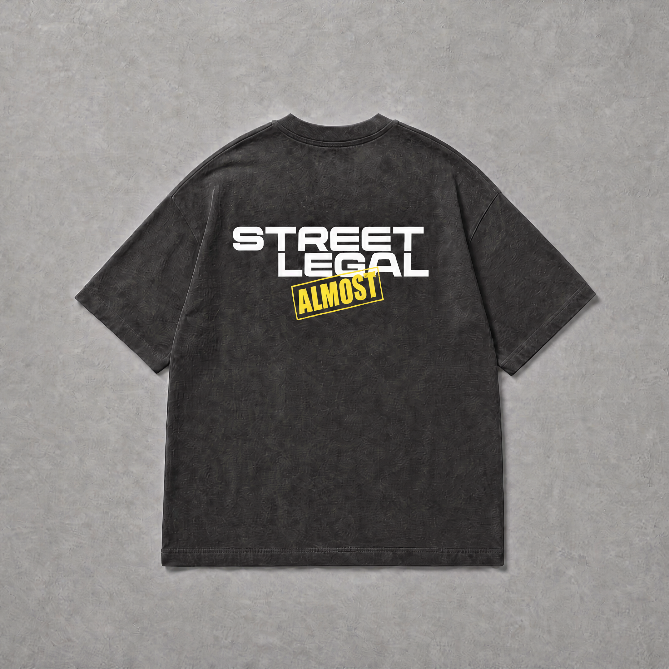 A dark gray mineral-wash t-shirt shown from the back, featuring a graphic print that reads 'STREET LEGAL' in white and 'ALMOST' in yellow. The t-shirt is laid flat on a textured gray background.